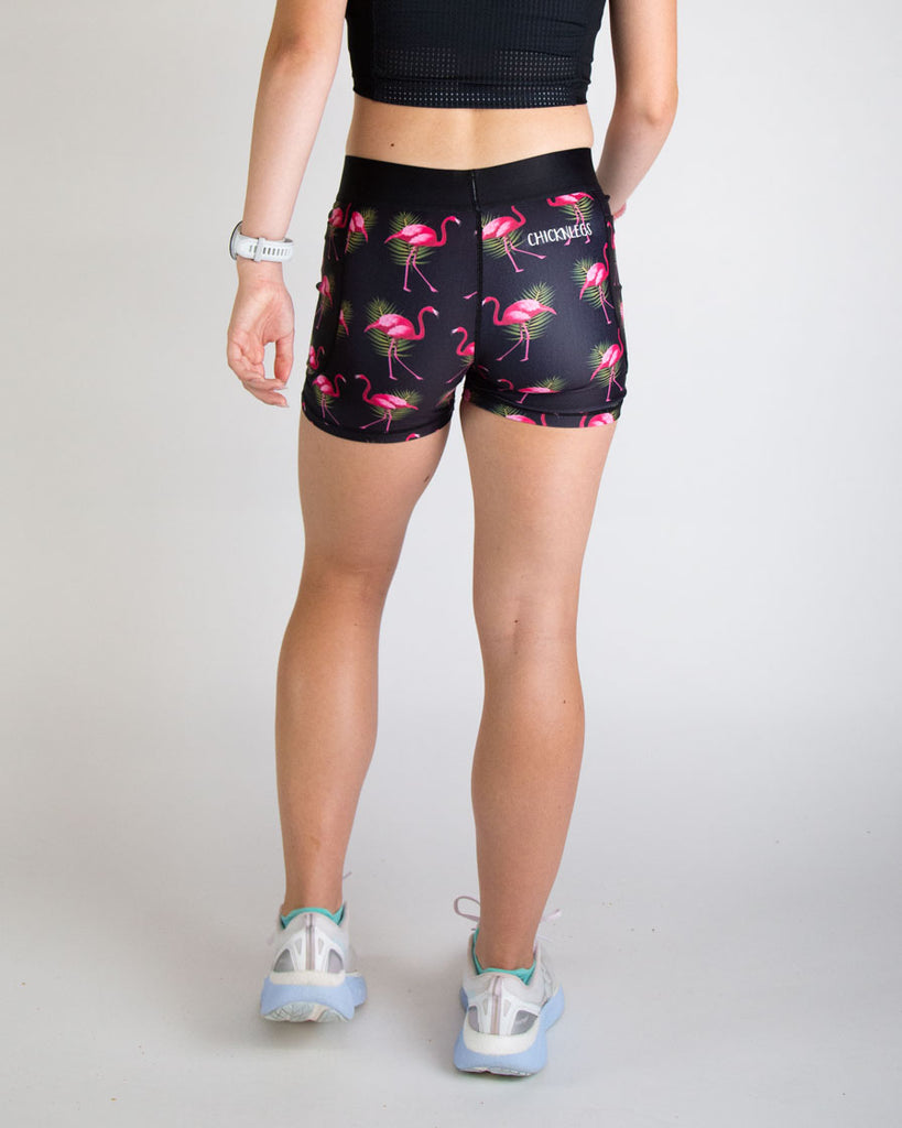 Runner is wearing ChicknLegs in the women's 3 in compression spandex shorts in the black flamingo design. The print has bright pink flamingos on it with green leaves on a black background. Back view is shown of the compressions to show the seam in the back.