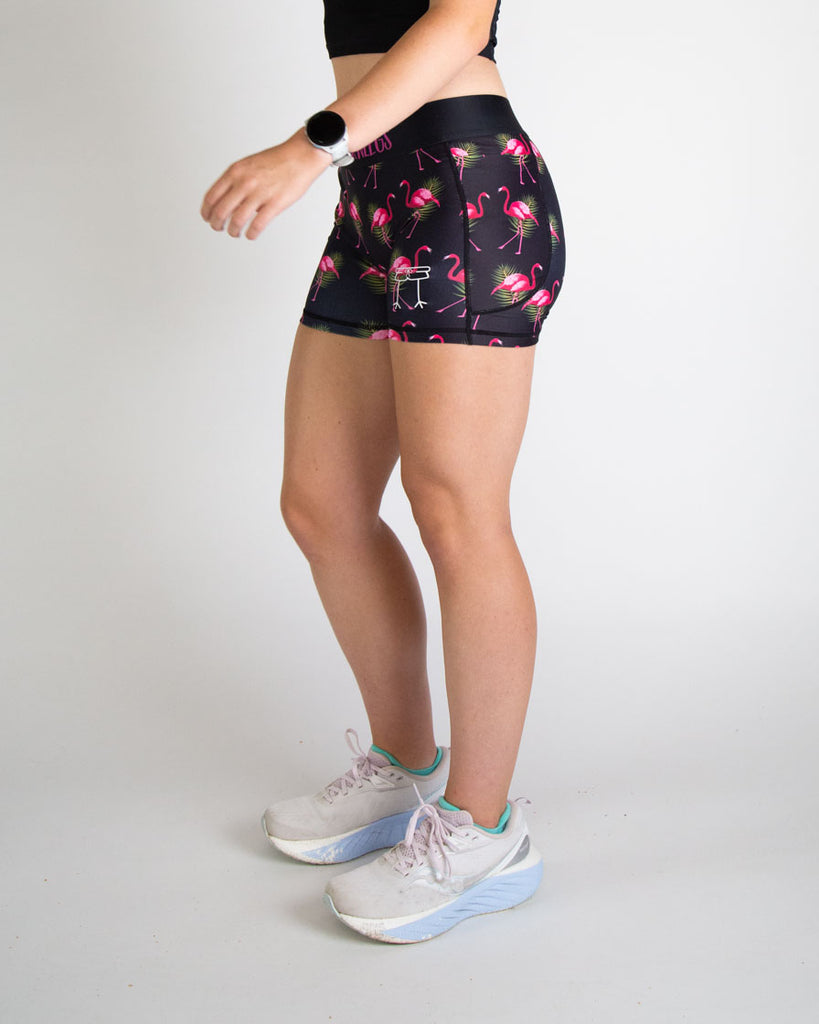 Runner is wearing ChicknLegs in the women's 3 in compression spandex shorts in the black flamingo design. The print has bright pink flamingos on it with green leaves on a black background. The sides have pockets on them for phones, keys, and more!