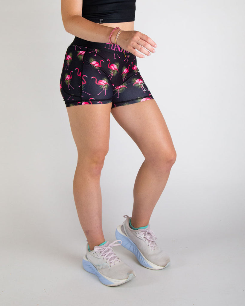 Runner is wearing ChicknLegs in the women's 3 in compression spandex shorts in the black flamingo design. The print has bright pink flamingos on it with green leaves on a black background. Great for workouts, runs, lifting, and hiking!
