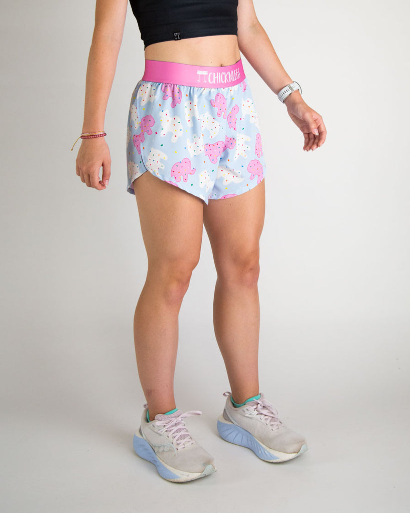 Runner is wearing Chicknlegs in the women's 4 in split running shorts in the frosted animal cookies print. The design has white and pink bright cookies with sprinkles on it. 