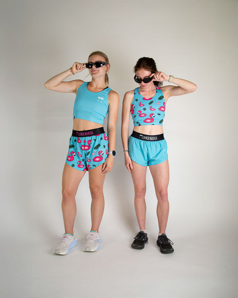 Runner is wearing ChicknLegs in the women's 1.5 in split running shorts in the solid color, sky blue design. Another model is shown wearing a matching fit with the sky blue crop top and blue flamingo print to match.