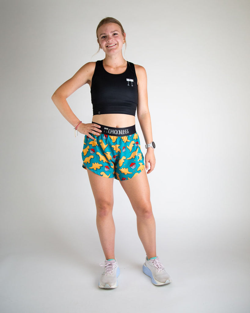 Runner is wearing ChicknLegs in the women's 4 in split running shorts in the dino nuggets design. The print has dinosaur chicken nuggets on it with ketchup on a blue background. Great length for all ages of women.