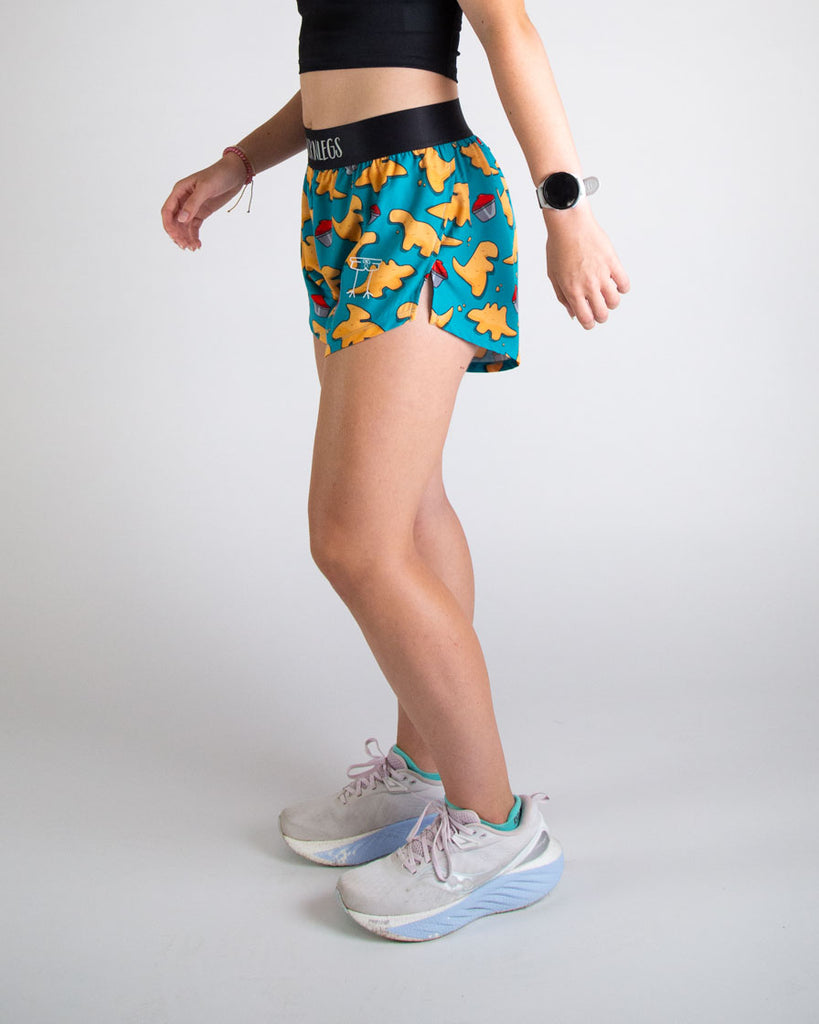 Runner is wearing ChicknLegs in the women's 4 in split running shorts in the dino nuggets design. The print has dinosaur chicken nuggets on it with ketchup on a blue background. These shorts are great for matching with the dino nugget crops and bras.