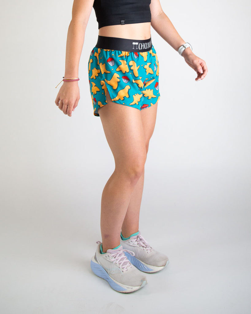 Runner is wearing ChicknLegs in the women's 4 in split running shorts in the dino nuggets design. The print has dinosaur chicken nuggets on it with ketchup on a blue background. Great for hiking, running, track and field, working out and weightlifting.