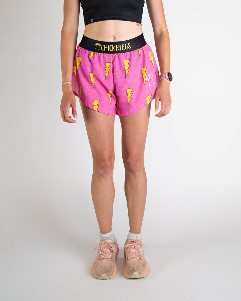 Runner is wearing ChicknLegs in the women's 4 in split running shorts in the hot pink bolts design. The print has a bright neon pink background with yellow electric lightning bolts.