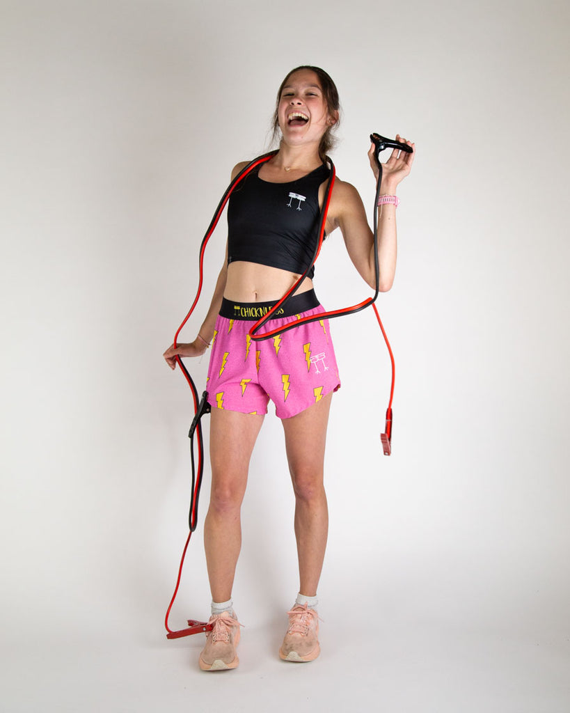 Runner is wearing ChicknLegs in the women's 4 in split running shorts in the hot pink bolts design. The print has a bright neon pink background with yellow electric lightning bolts. 