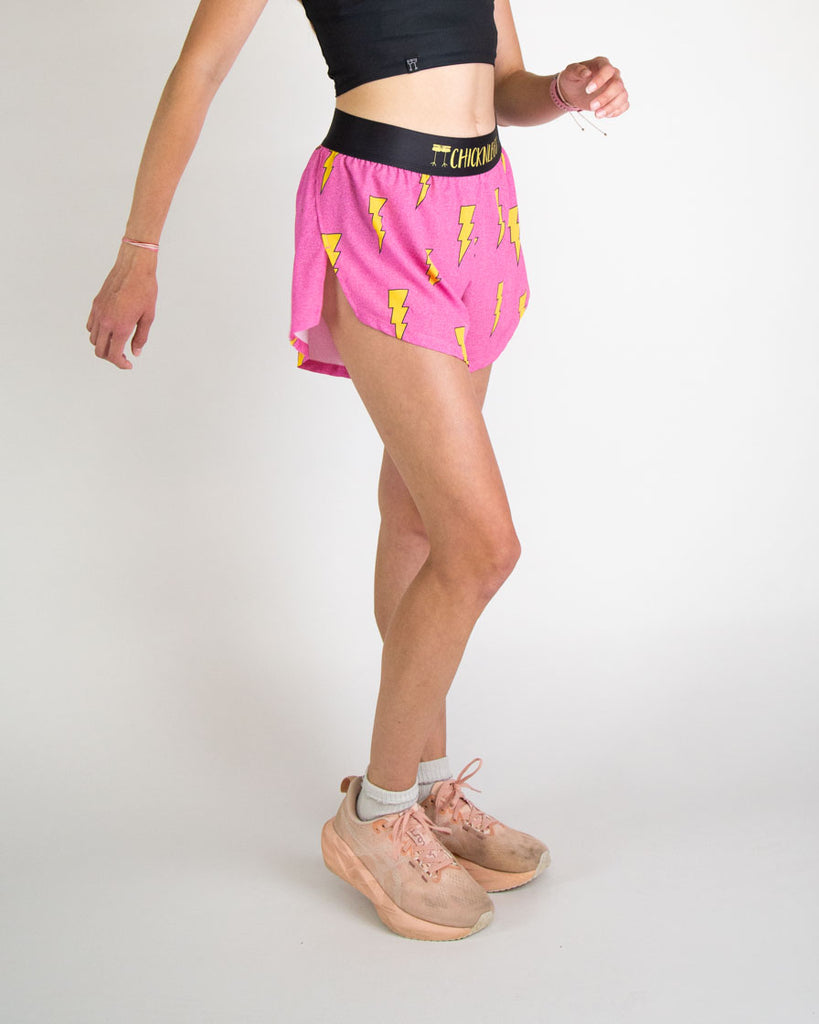 Runner is wearing ChicknLegs in the women's 4 in split running shorts in the hot pink bolts design. The print has a bright neon pink background with yellow electric lightning bolts.