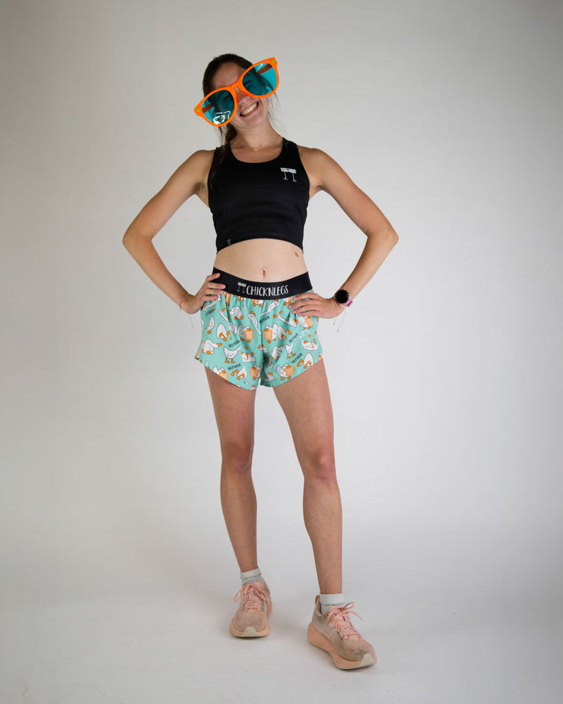 Runner is wearing ChicknLegs in the women's 4 in split running shorts in the silly goose design. The print has white, orange and blue on it with a bunch of geese. A full body image is shown of the model wearing fun bright big sunglasses.