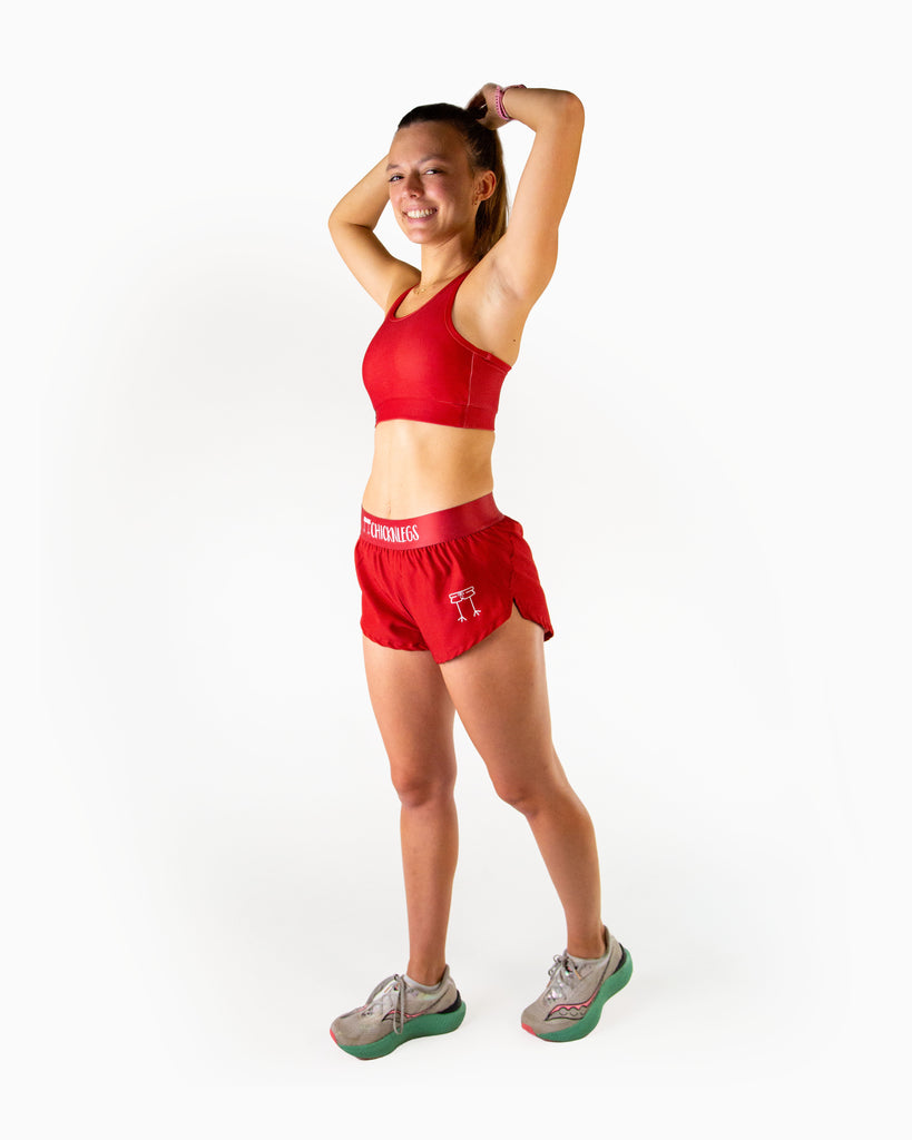 Full body view of model wearing ChicknLegs women’s 1.5-inch split running shorts in solid cardinal red, styled with matching cardinal red og sports bra and white running shoes.
