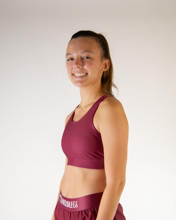 Left side view of ChicknLegs women’s OG sports bra in solid maroon, showing racerback strap and supportive fit.