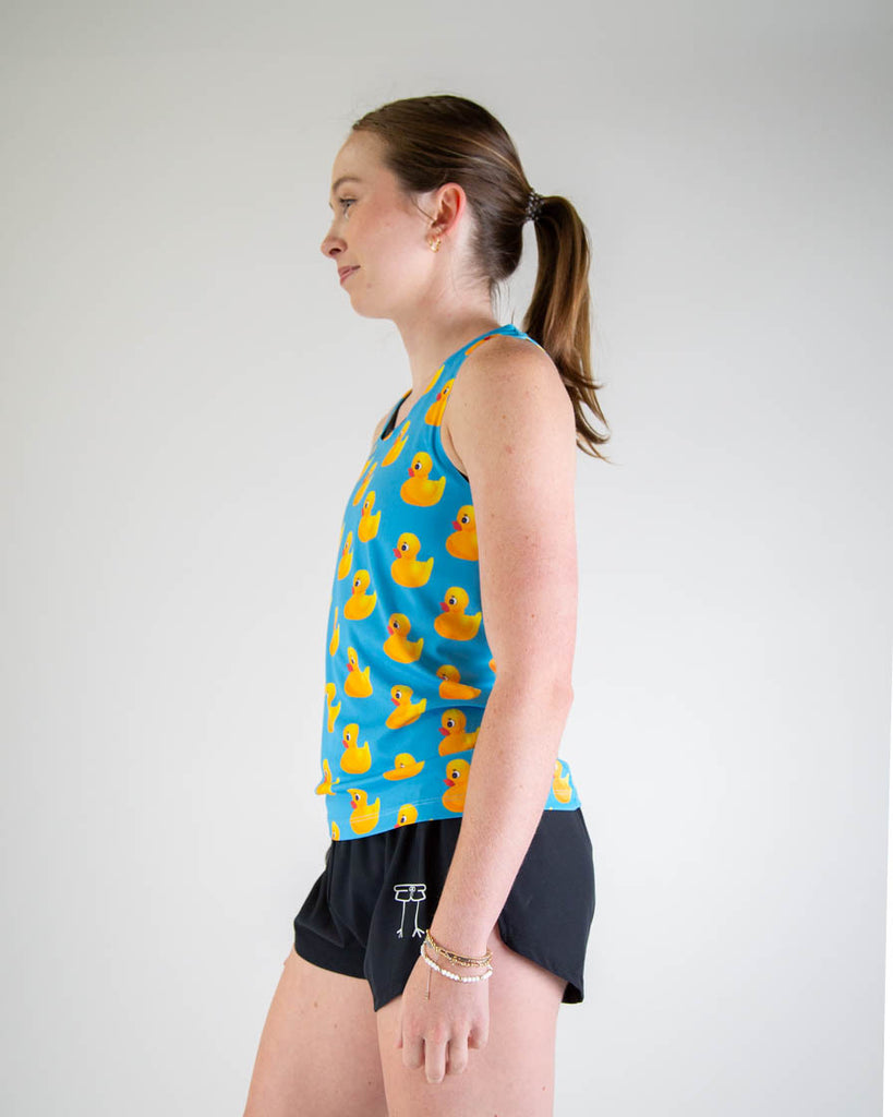 Left side view of ChicknLegs women’s performance running singlet. Blue background with yellow rubber ducky's all over, paired with black running shorts.