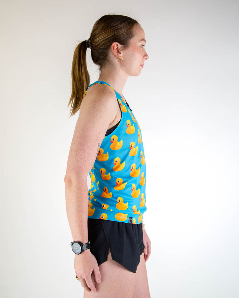 Right side view of ChicknLegs women’s performance running singlet. Blue background with yellow rubber ducky's all over. Paired with black shorts.