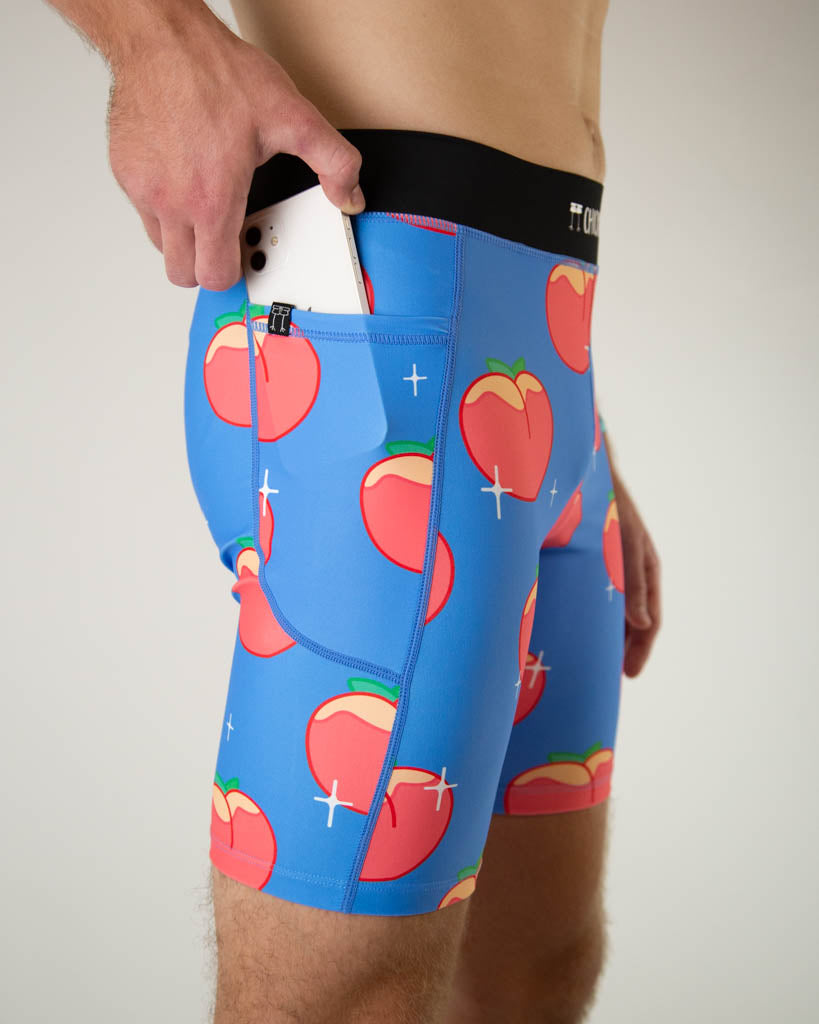 A close up photo of ChicknLegs men’s 8-inch half tights, breathable liner, blue background and juicy peaches design. Runner is holding a phone while putting it in the pocket.