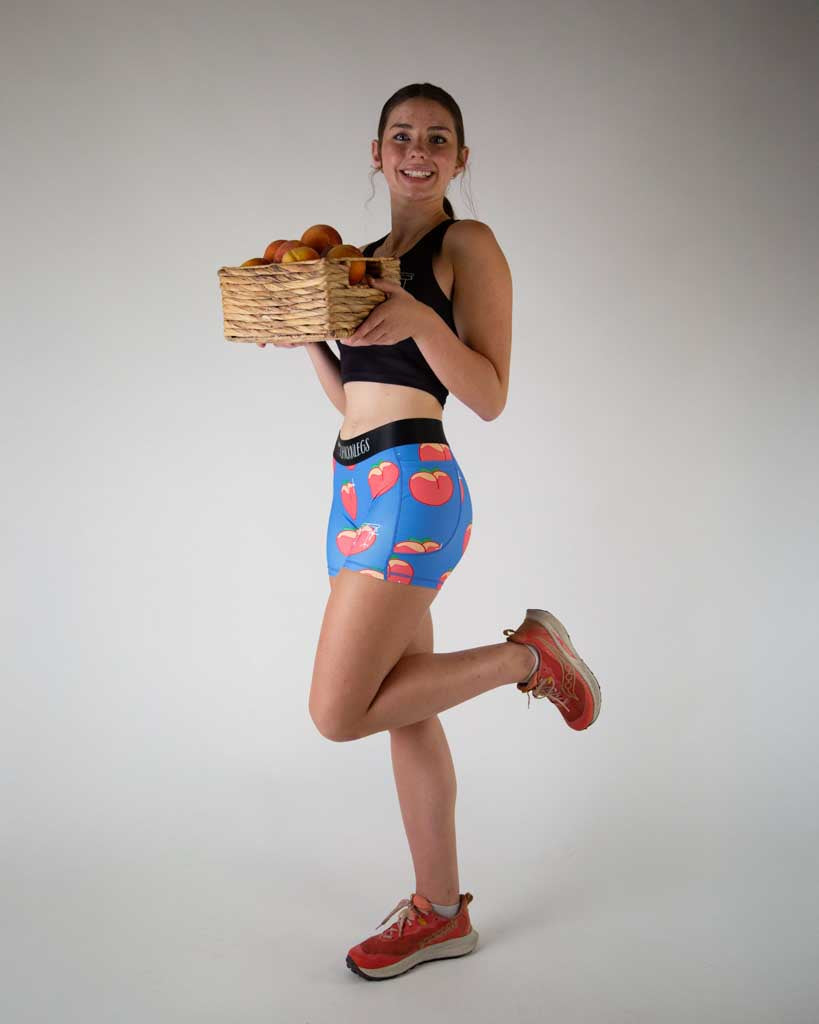 Full body view of ChicknLegs women’s 3-inch compression spandex shorts, black non chaffing waistband, blue background and juicy peaches on the design.