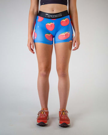Front view of ChicknLegs women’s 3-inch compression spandex shorts, black non chaffing waistband, blue background and juicy peaches on the design.