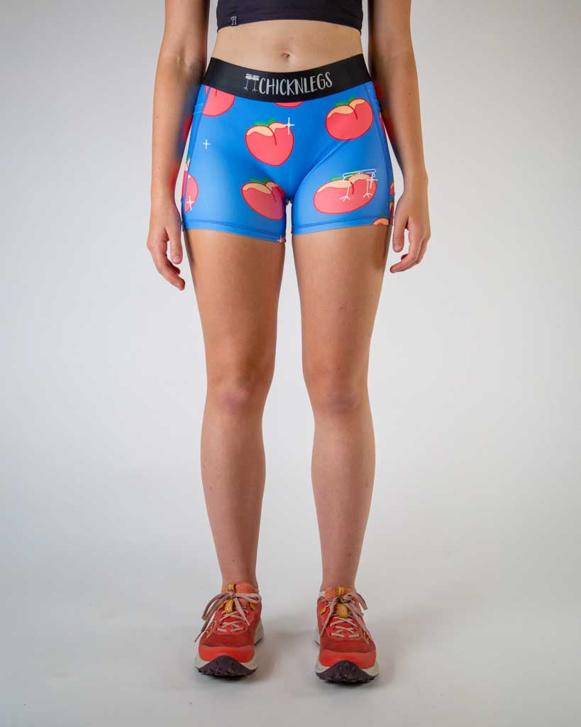 Front view of ChicknLegs women’s 3-inch compression spandex shorts, black non chaffing waistband, blue background and juicy peaches on the design.