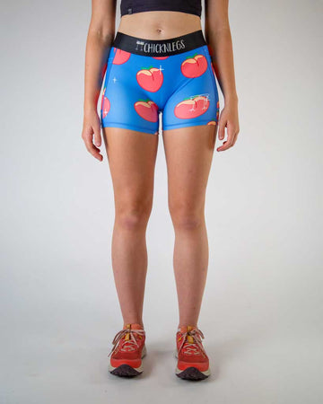Front view of ChicknLegs women’s 3-inch compression spandex shorts, black non chaffing waistband, blue background and juicy peaches on the design.