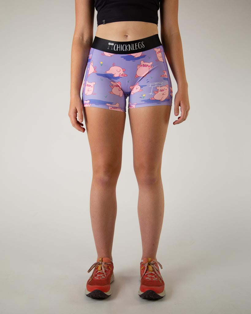 Front view of ChicknLegs women’s 3-inch compression spandex with side pockets, lilac purple background and pink piggies design.