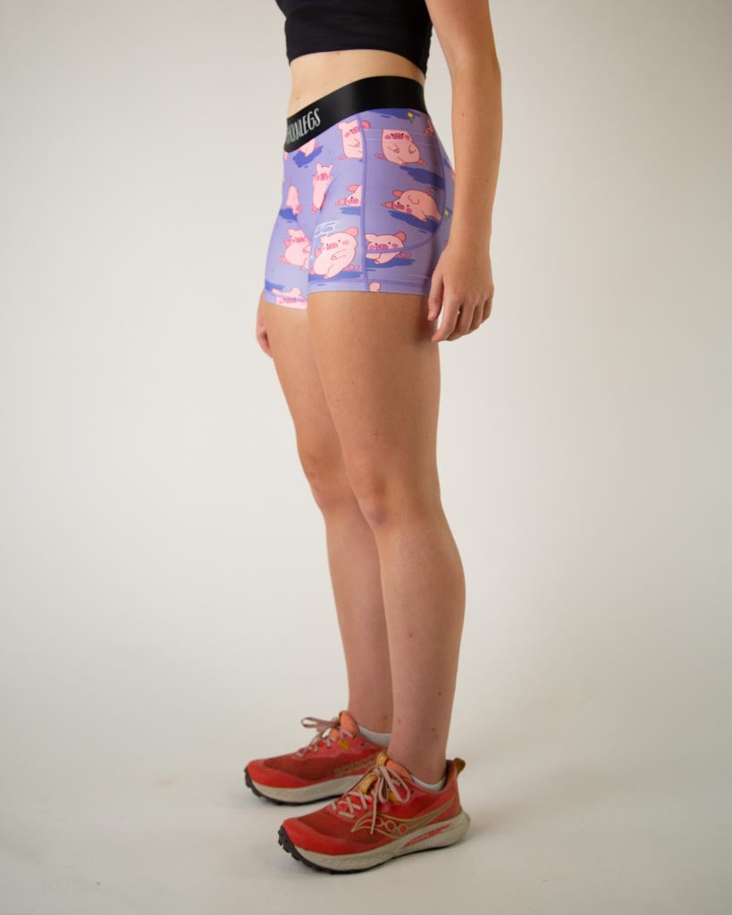 Left side view of ChicknLegs women’s 3-inch compression spandex with side pockets, lilac purple background and pink piggies design.