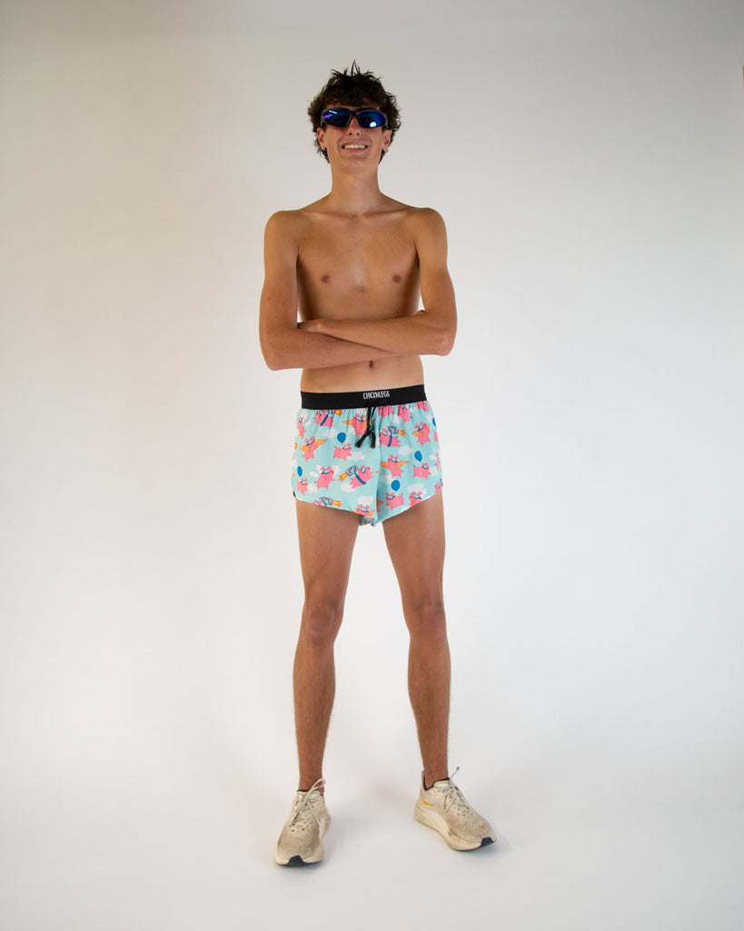Runner is wearing ChicknLegs in the men's 2 in drawstrings in the split running shorts in the flying pig design. The model is posing while wearing goggles like the flying pigs are wearing.