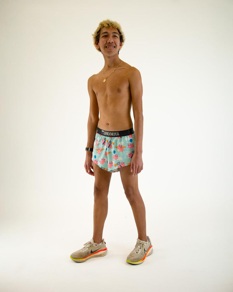 Runner is wearing ChicknLegs in the men's 2 in split running shorts in the flying pigs design. The print has pink piggies on it with goggles, cardboard, wings, and jetpacks the model is in a walking stance. 