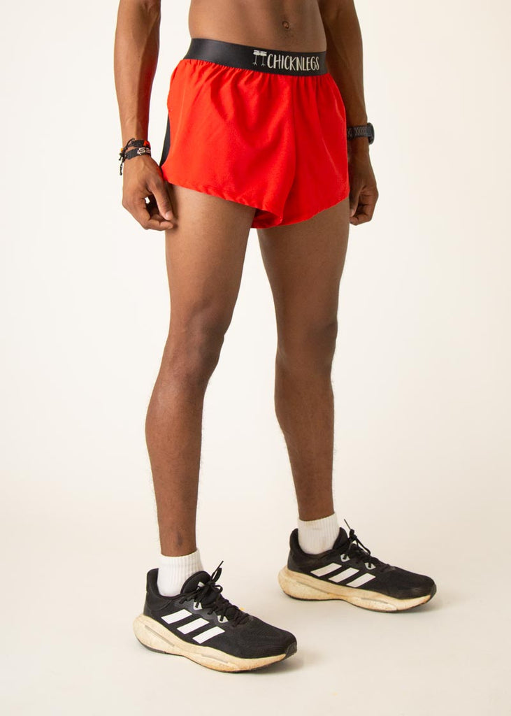 Model is wearing Chicknlegs mens 2 inch split running shorts in the red design, facing right.