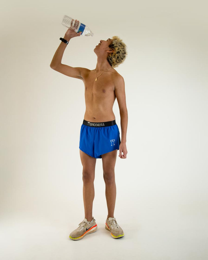 Runner is wearing ChicknLegs in the men's 2 in split running shorts in the royal blue design, posing and holding water.
