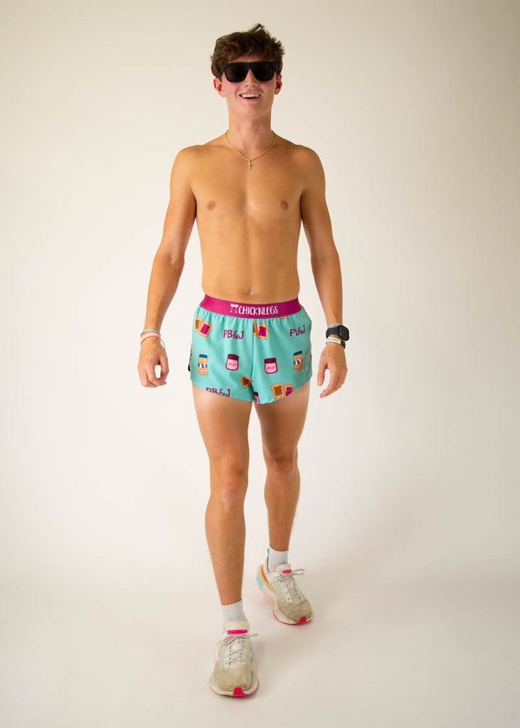 The model is a runner that is wearing athletic Chicknlegs men's 2 inch split running shorts in the PB&J design that includes PB&J sandwiches, peanut butter, jelly on a light blue background, facing front while in a walking athletic pose.