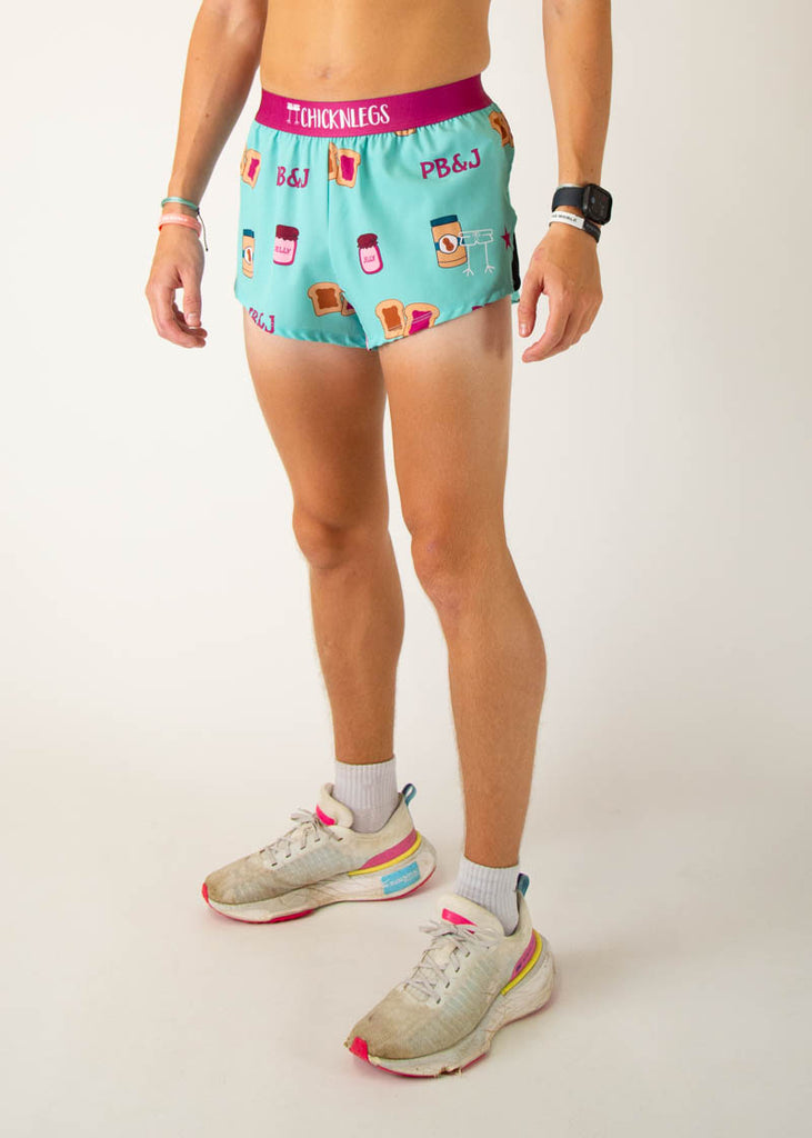 The model is a runner that is wearing athletic Chicknlegs men's 2 inch split running shorts in the PB&J design that includes PB&J sandwiches, peanut butter, jelly on a light blue background, facing left.
