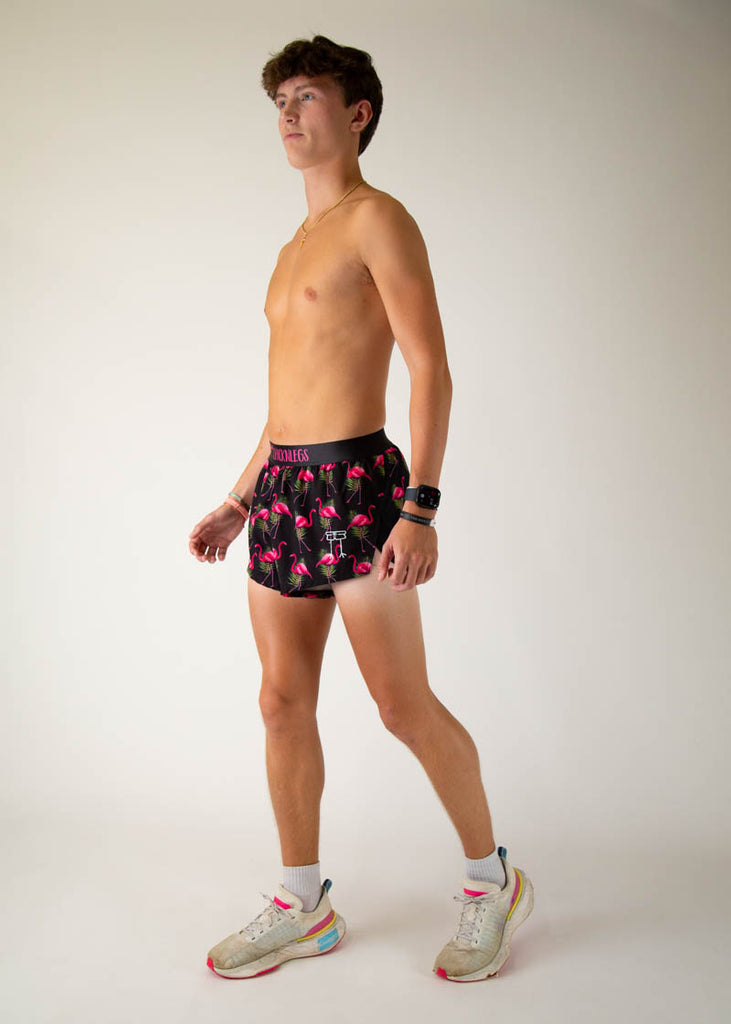 Model is a runner wearing Chicknlegs men's 2 inch split running shorts in the black flamingo design, facing left in a walking stance showing the full body of the model.