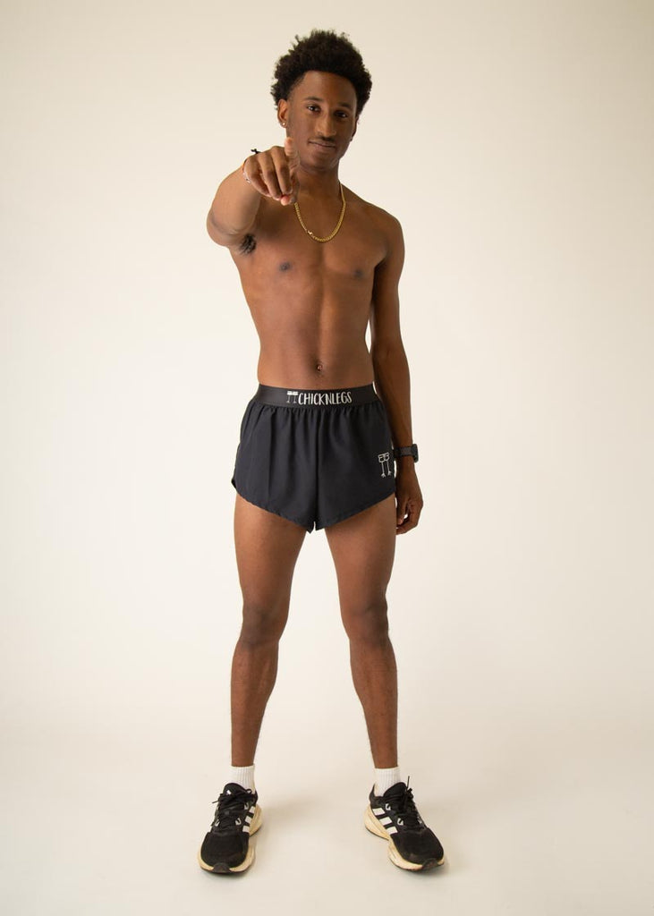 Model is wearing Chicknlegs in the mens 2 inch split running shorts in the black design, facing front while posing and pointing at the camera.
