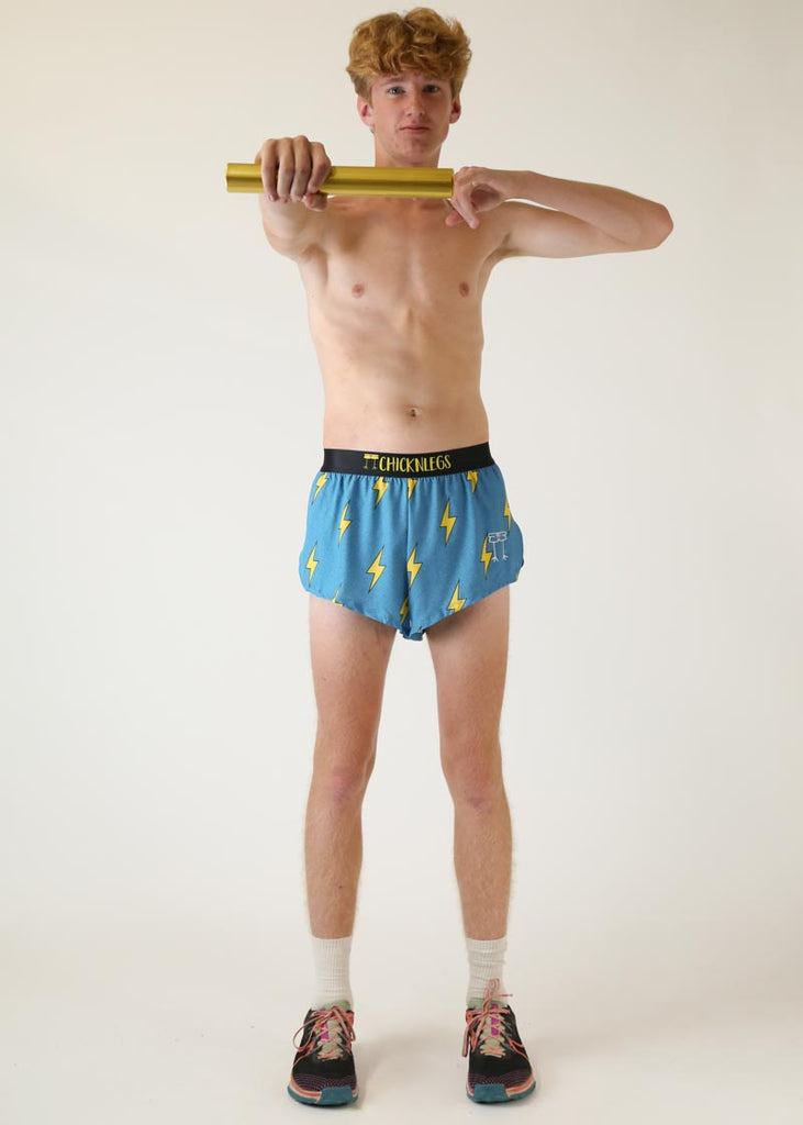 Model wearing chicknlegs mens 2 inch split running shorts with blue bolts design full body view while holding baton