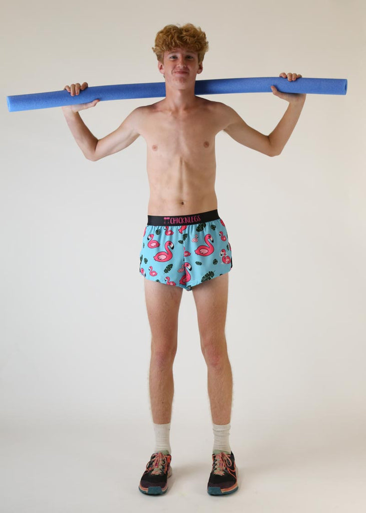 Model wearing Chicknlegs men's 2 inch split running shorts in blue flamingo design holding pool noodle