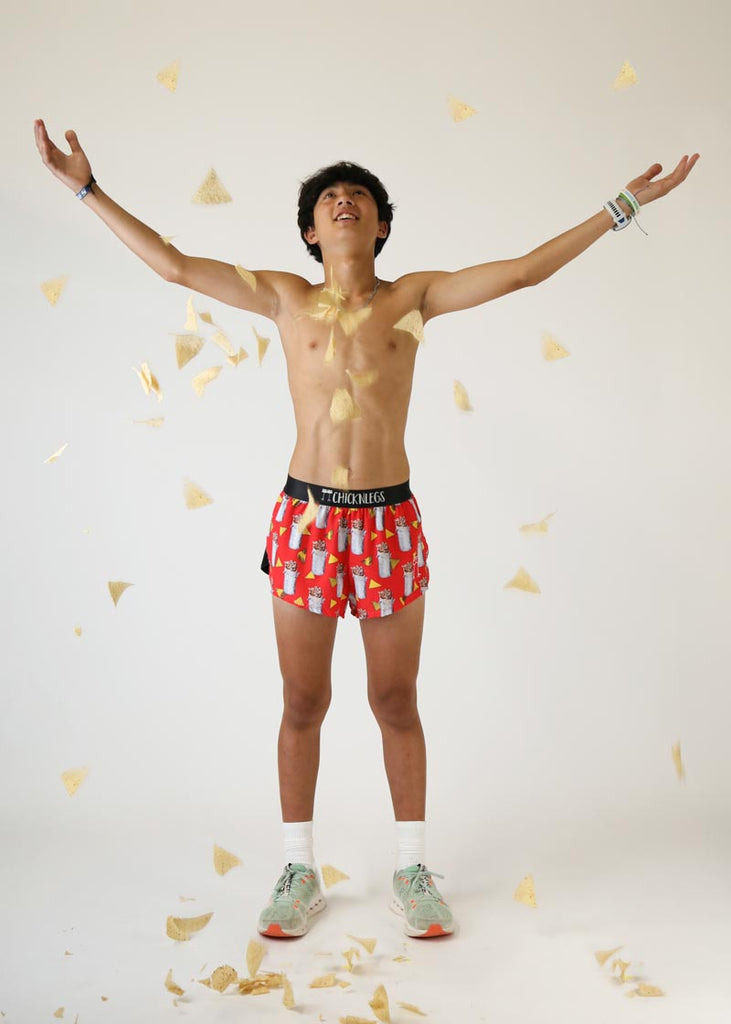 Model wearing Chicknlegs men's 2 inch split running shorts in the burrito design throwing chips into the air