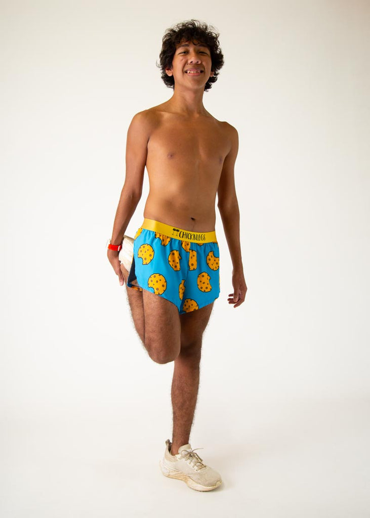 The model is a runner who is wering Chicknlegs in men's 2 inch split running shorts in the cookies design, posing while stretching their quad.