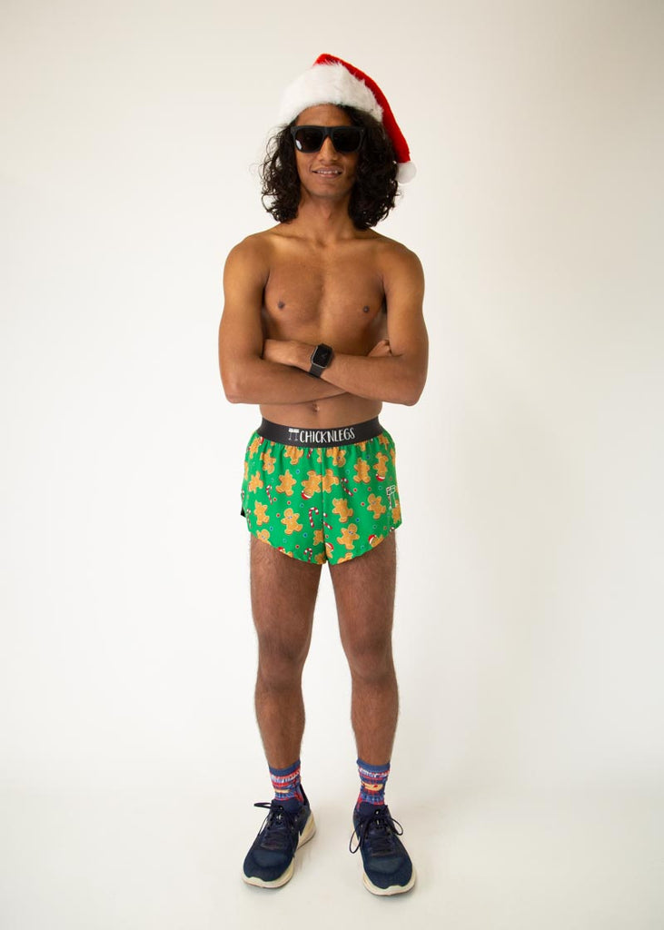 The model is a runner who is wearing Chicknlegs men's 2 inch split running shorts in the Gingerbread Men's Gingy Revenge design, facing front while posing and crossing their arms wearing a santa hat.