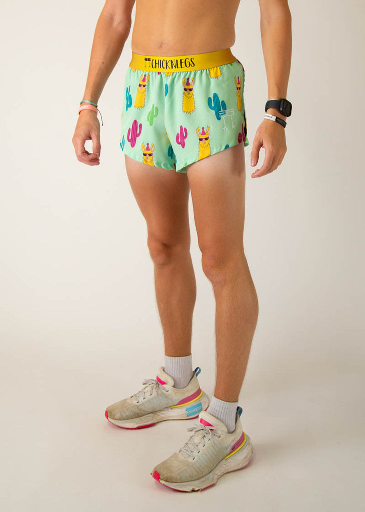 The model is a runner wearing Chicknlegs in men's 2 inch split running shorts in the green llama design, facing left.
