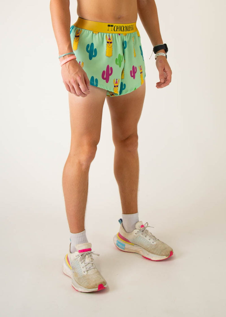 The model is a runner wearing Chicknlegs in men's 2 inch split running shorts in the green llama design, facing right.
