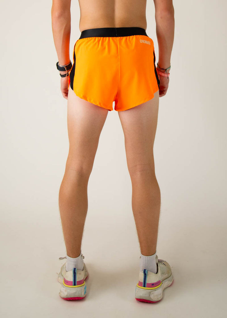 The model is a runner wearing Chicknlegs men's 2 inch split running shorts in the neon orange design, facing away from the camera to show the back of the shorts.
