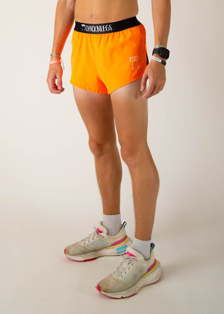 The model is a runner wearing Chicknlegs men's 2 inch split running shorts in the neon orange design, facing left.
