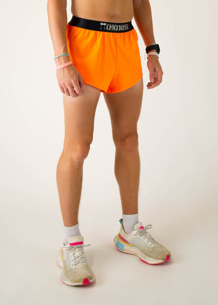 The model is a runner wearing Chicknlegs men's 2 inch split running shorts in the neon orange design, facing right.

