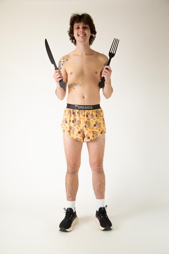The model is a runner who is wearing Chicknlegs in men's 2 inch split running shorts in the pardoned turkey design, facing front while posing with a fork and a knife.