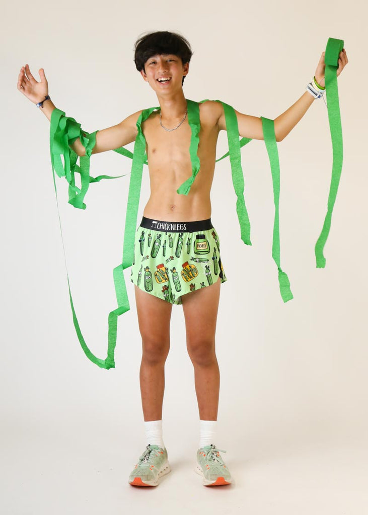 Model wearing Chicknlegs mens 2 inch split running shorts in pickles design while holding streamers as a full body view