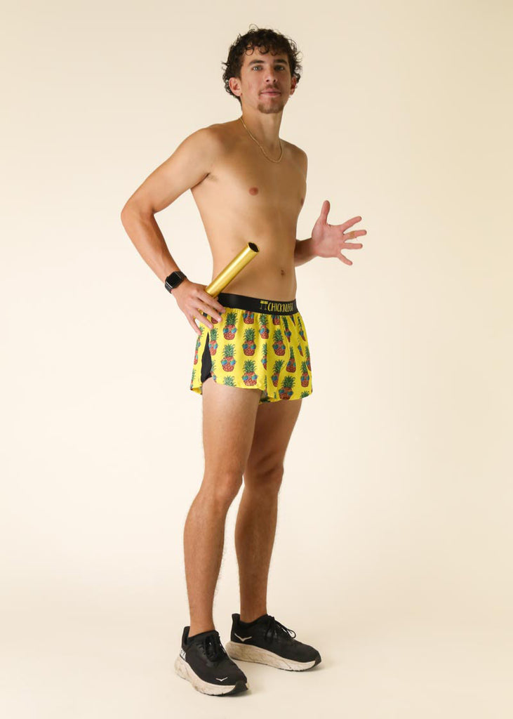 Runner is wearing ChicknLegs in the men's 2 in split running shorts with the pineapple express design. Full body shot is shown while working out and using a baton.