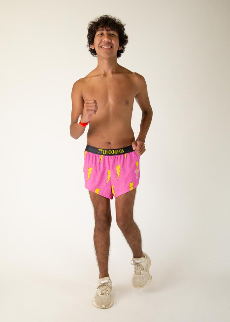 The model is a runner who is wearing Chicknlegs men's 2 inch split running shorts in the pink bolts design, facing front while running in place.