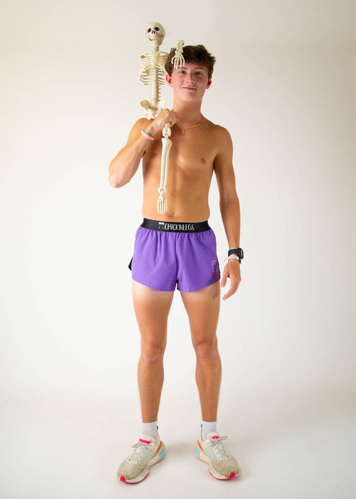 The model is a runner wearing Chicknlegs men's 2 inch split running shorts in the purple design, facing front while posing with a skeleton on their shoulder.