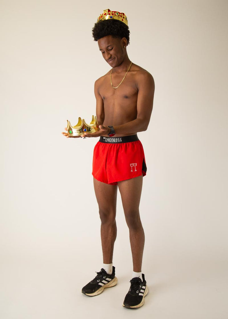 Model is wearing Chicknlegs mens 2 inch split running shorts in the red design, facing front while posing and wearing a red crown.
