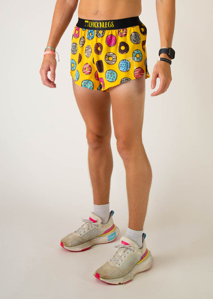 The model is a runner that is wearing Chicknlegs men's 2 inch split running shorts in the salty donuts design, facing left.
