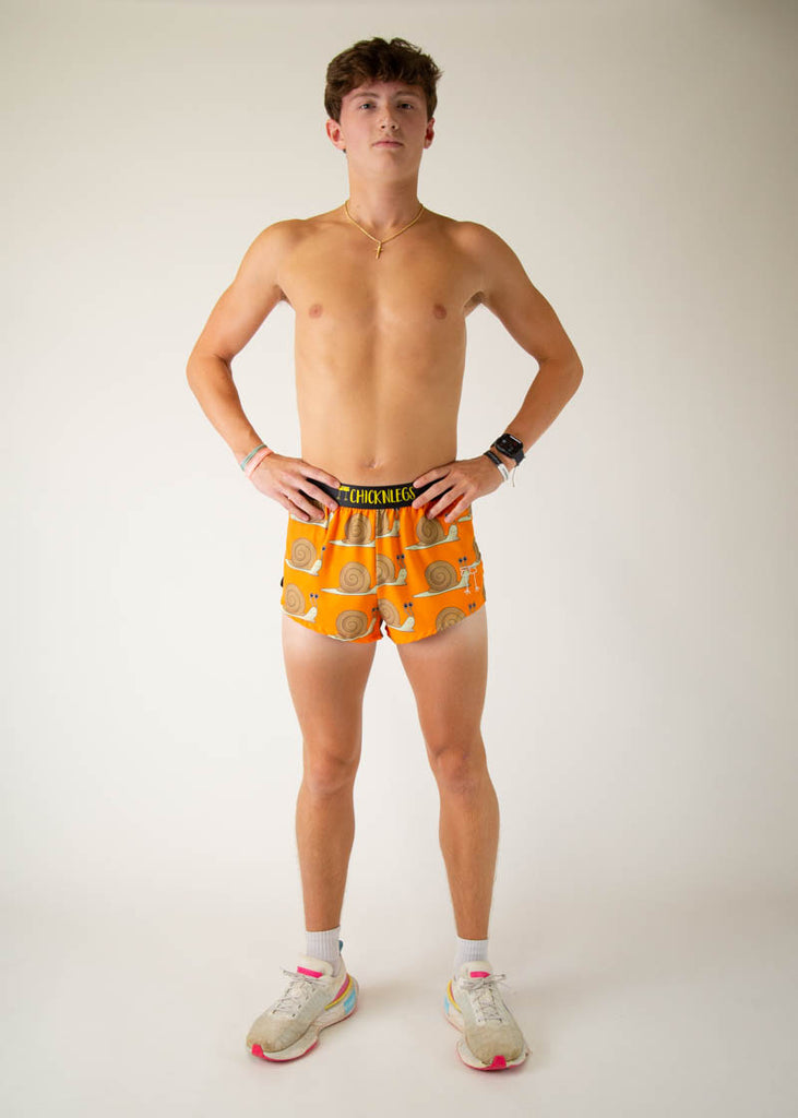 The model is a runner wearing Chicknleg's men's 2 inch split running shorts in the snails design, facing front while posing with their hands on their waist, showing off the shorts.