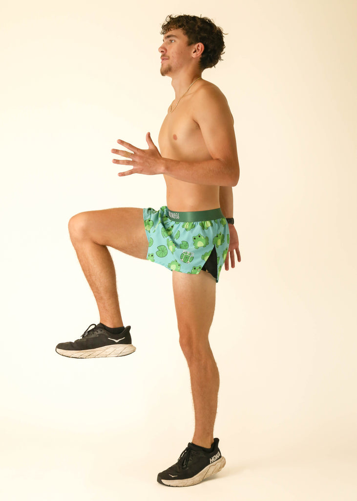 Model is a runner wearing athletic shorts made by Chicknlegs in the men's 2 inch split running shorts in the Fartlek Froggies Frog design, posing in a running stance.